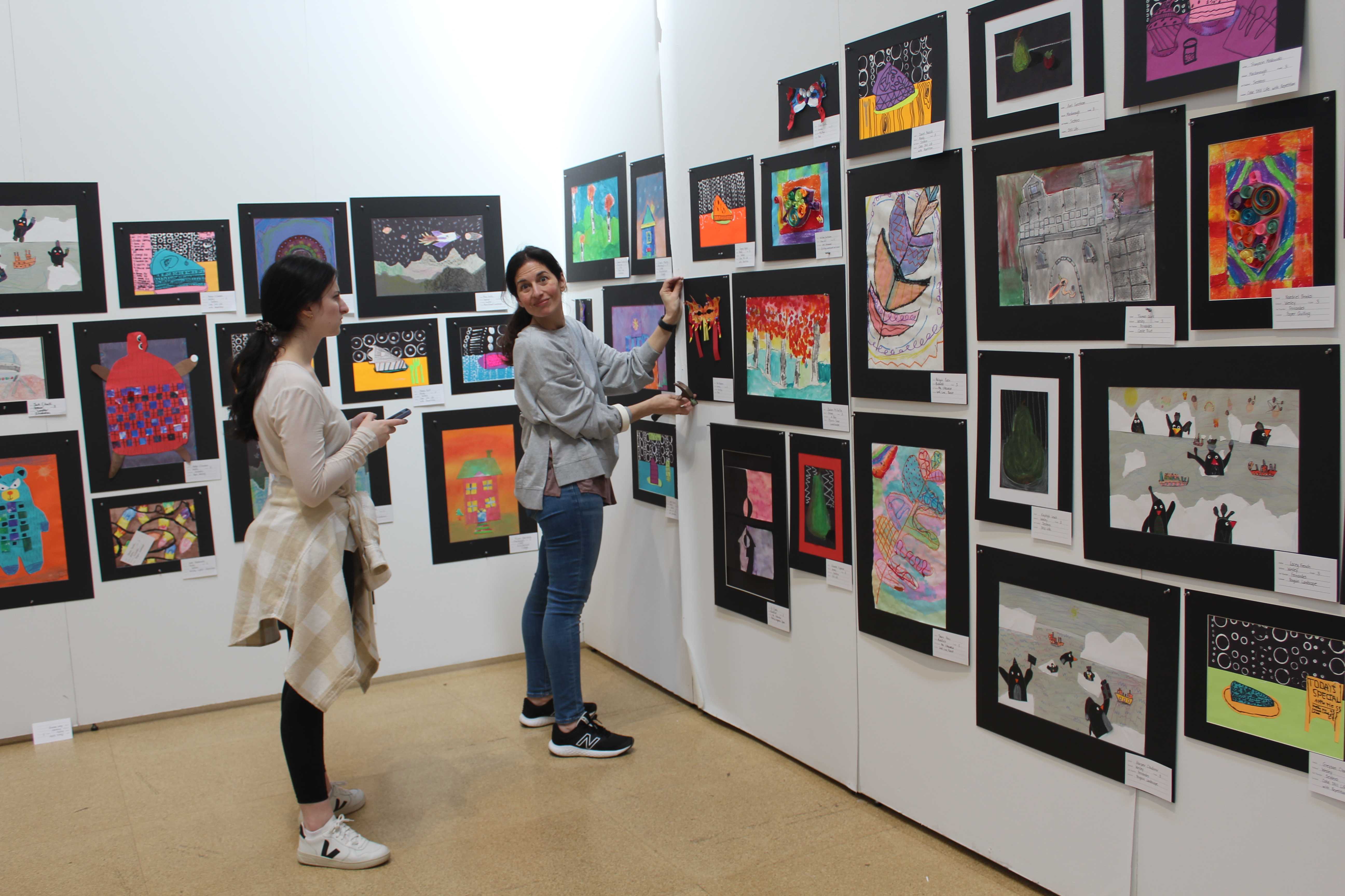 Students are putting up pieces of artwork at the gallery for the upcoming art show